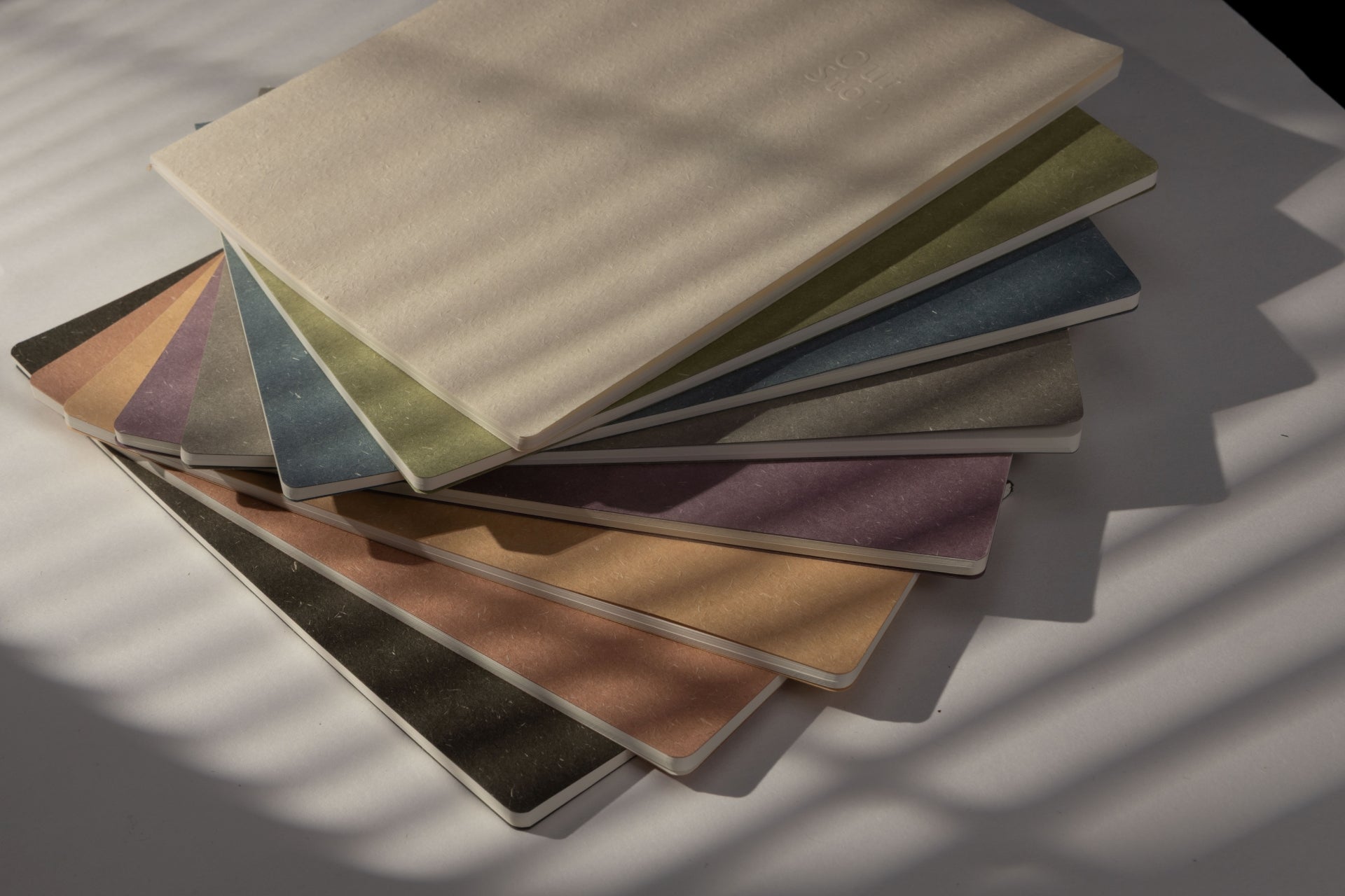 A stack of minimalist soft cover notebooks in various aesthetic earth tone colors, perfect stylish stationery supplies for college students and office desks
